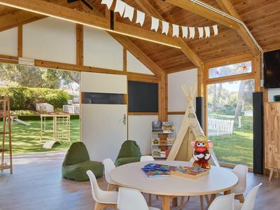 Lichte speelkamer voor kinderen met houten plafonds, ronde tafel, zitzakken en uitzicht op de tuin.