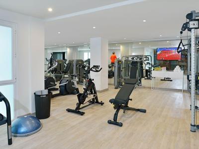 Ein heller Fitnessraum mit Trainingsgeräten, Gewichten und Spiegeln an den Wänden.