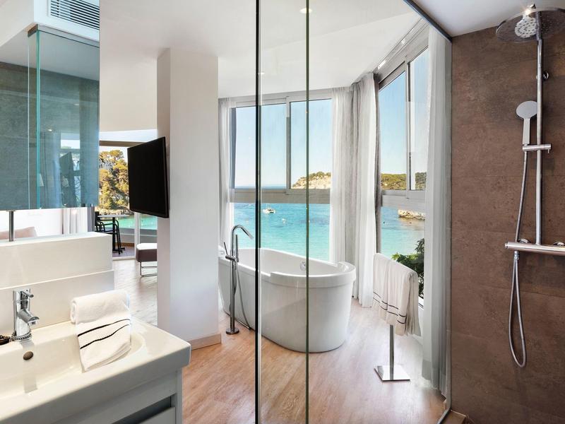 Lichte badkamer met vrijstaand bad en uitzicht op zee, moderne douche en wastafel.