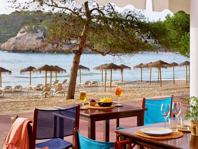 Tafel en stoelen met drankjes op een strand met parasols en bomen op de achtergrond