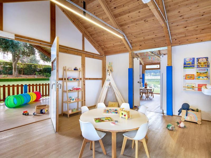 Lichte kinderspeelruimte met houten muren, speelgoed, tafel en stoelen in een hotel- of vakantieplek.