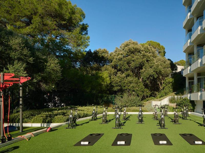 Buitensportgebied met fitnessapparaten op groen gras naast een hotelgebouw en bomen