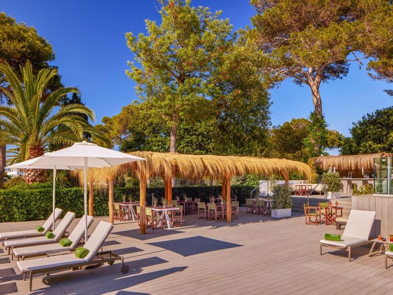 Buitengebied van een hotel met ligstoelen, parasols en een bar onder een rieten dak