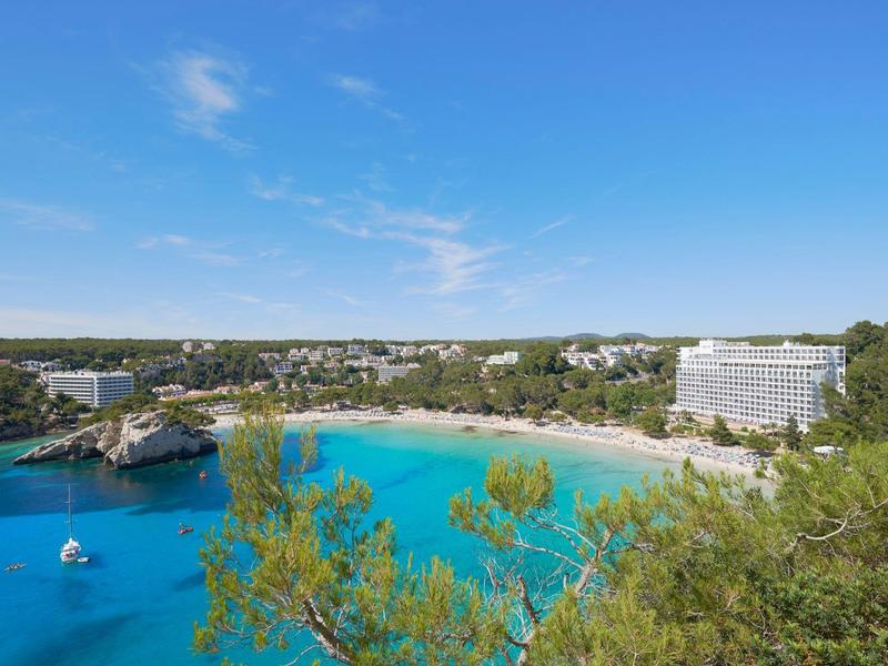 Strand en hotels langs een kust met helder blauw water en blauwe lucht.
