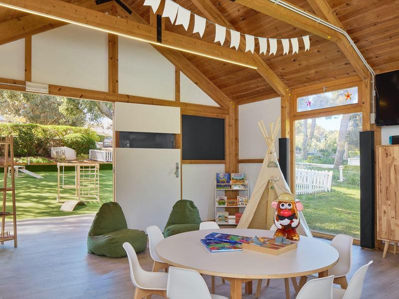 Lichte speelkamer voor kinderen met houten plafonds, ronde tafel, zitzakken en uitzicht op de tuin.