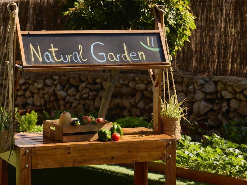 Houten tafel in de tuin met fruit, groenten en een bord met de tekst Natural Garden