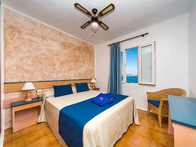 Habitación de hotel acogedora con cama doble, detalles en azul y vista al mar por la ventana abierta.