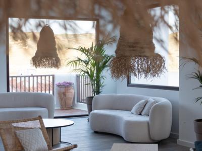 Área de estar moderna con sofás blancos, plantas y pantallas de lámparas tejidas.