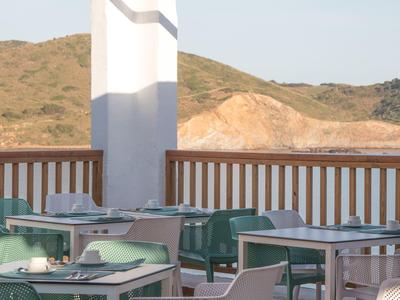 Terraza de hotel con mesas y sillas con vistas a colinas boscosas.