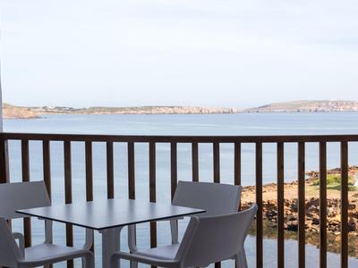 Vista desde un balcón con sillas y mesa hacia el mar y la costa rocosa.
