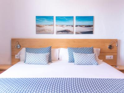 Dormitorio luminoso con cama grande, ropa de cama azul y blanca con estampado y fotos de playa sobre el cabecero.