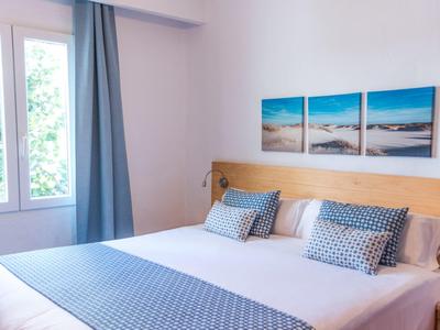 Dormitorio luminoso con cama grande, cortinas azules y tres cuadros de playa en la pared.
