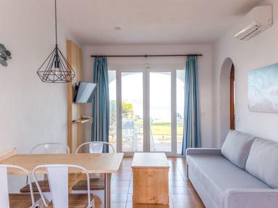 Sala luminosa con sofá gris, mesa de comedor, sillas y grandes ventanas con vista al exterior.