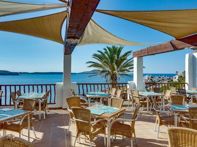 Terrazza di un hotel sulla spiaggia con tavoli, sedie e vista sul mare e una palma.