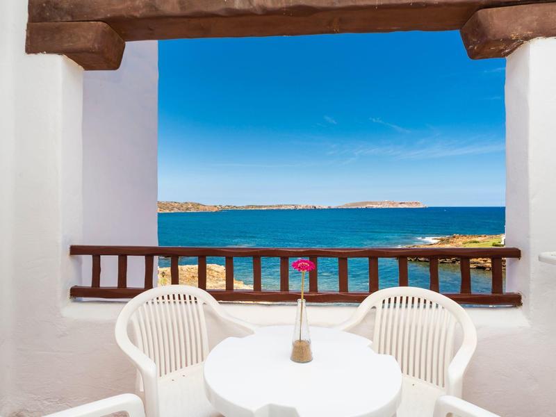 Balcón con mesa y sillas blancas con vista al mar y cielo azul.