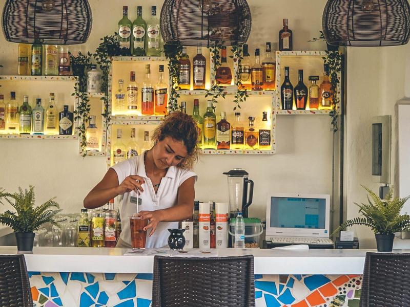 Barman preparando bebidas en un bar decorativo con plantas y botellas.