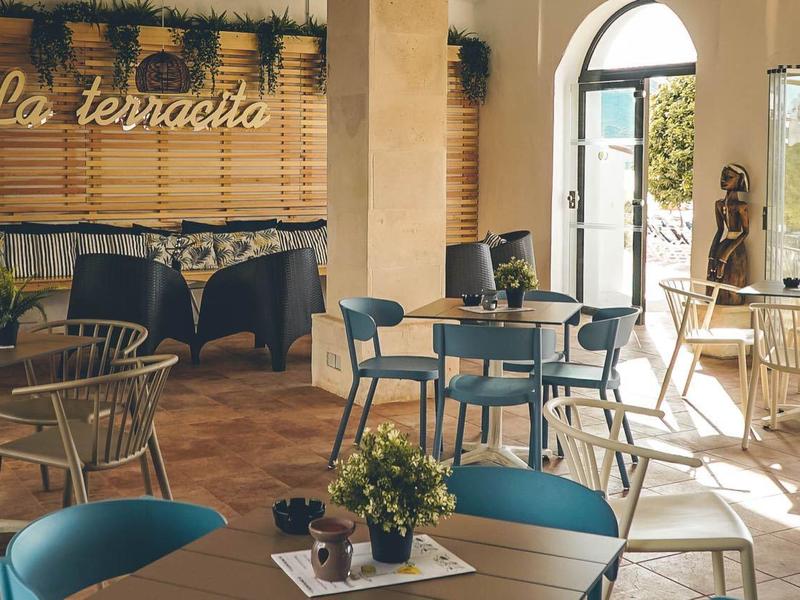 Cafetería luminosa amueblada con mesas y sillas junto a grandes ventanas con vista a la naturaleza.