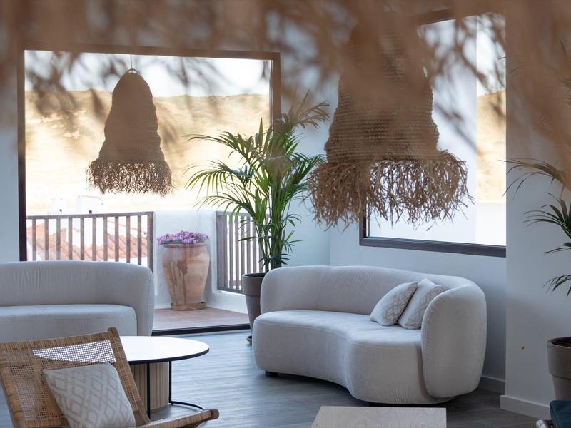 Área de estar moderna con sofás blancos, plantas y pantallas de lámparas tejidas.