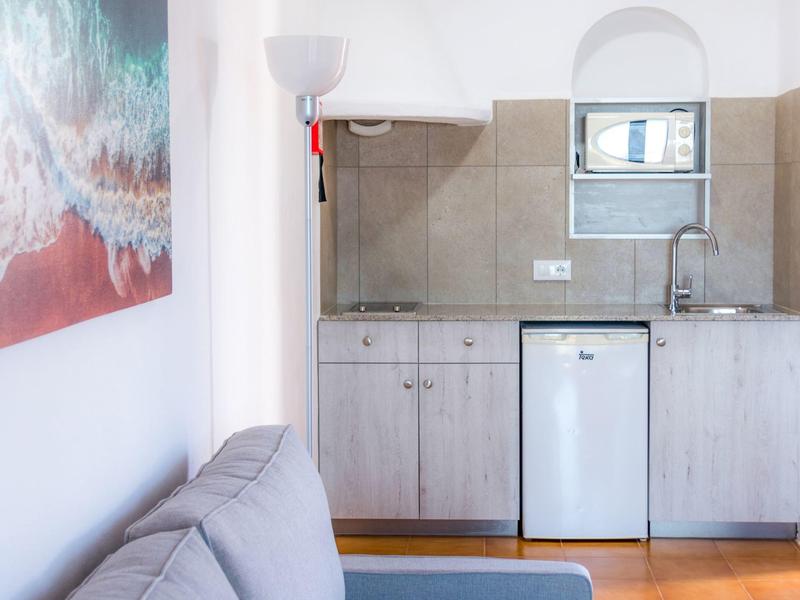 Pequeña kitchenette con nevera junto a un sofá gris y una obra de arte en la pared.