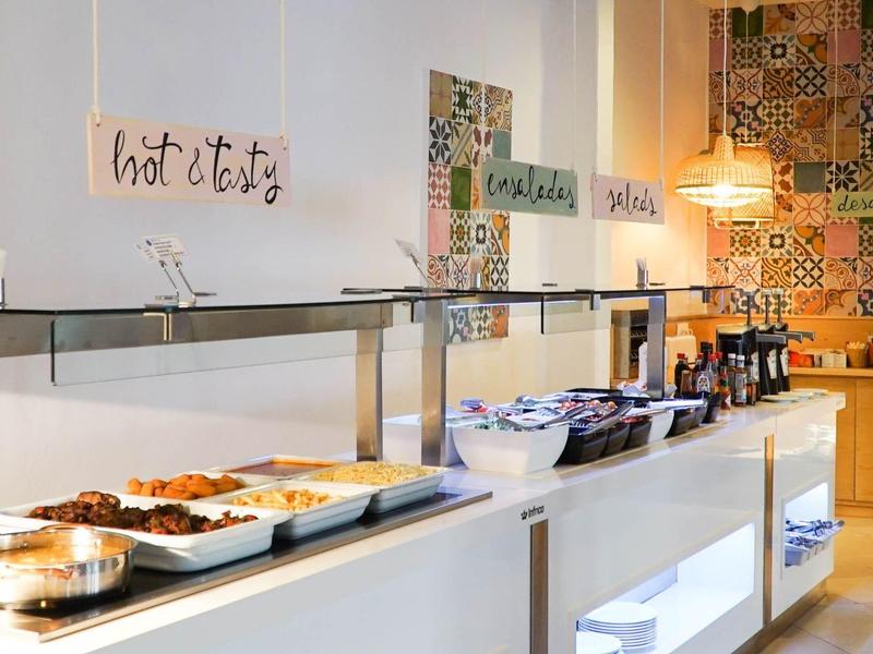 Buffet de desayuno moderno con diversos platos y máquinas de bebidas calientes en un hotel.