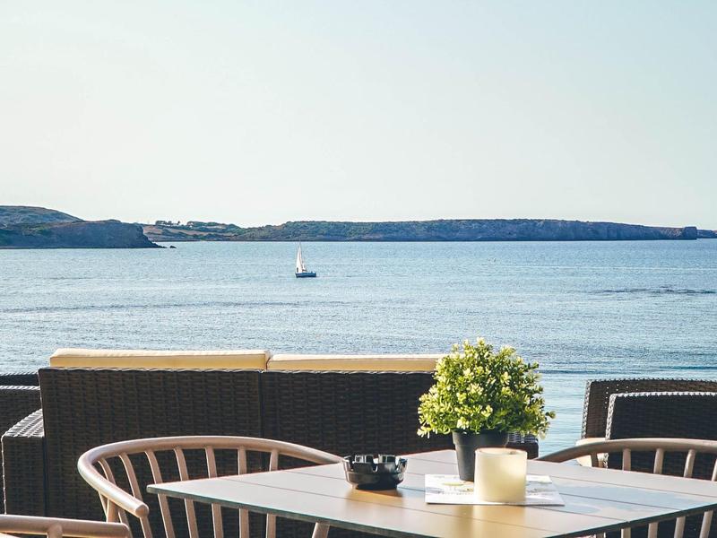 Una mesa con velas y sillas con vista al mar y a islas distantes.
