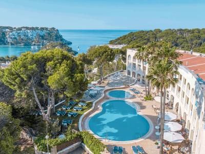 Hotelanlage mit mehreren Pools, umgeben von Palmen und Blick aufs Meer.