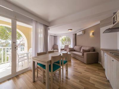 Helles Wohnzimmer mit Esstisch, Sofa und Balkon mit Blick auf Bäume und Gebäude.