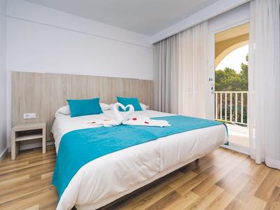 Modernes Doppelbett mit türkisfarbener Bettdecke und Balkonblick durch große Fenster.