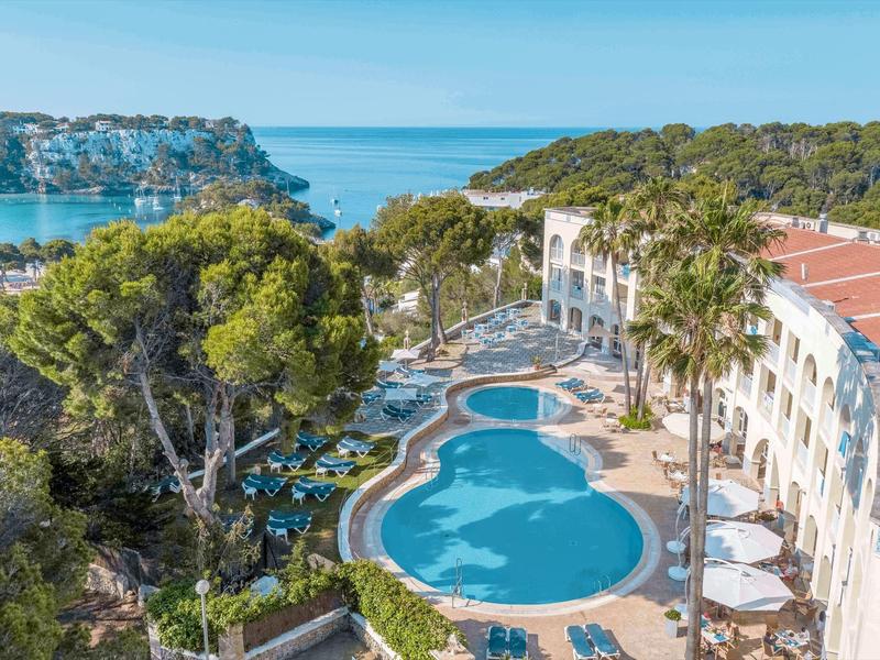 Hotelanlage mit mehreren Pools, umgeben von Palmen und Blick aufs Meer.