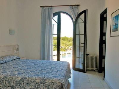 Helles Schlafzimmer mit großen französischen Türen, blauen Vorhängen und Bett mit gemustertem Bettbezug.