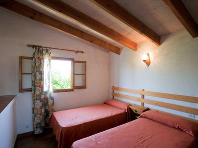 Kleines Schlafzimmer mit zwei Einzelbetten, Holzbalken an der Decke und geöffnetem Fenster mit Blumen-Vorhang.