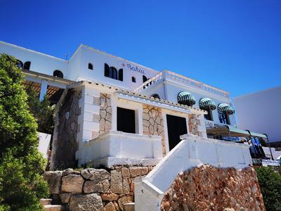 Weißes Steingebäude mit Treppe und Pflanzen vor strahlend blauem Himmel.