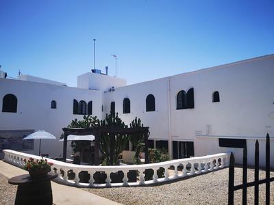 Weißes Gebäude mit schwarzen Fenstern, Kakteengarten und weißem Balkongeländer unter klarem Himmel.