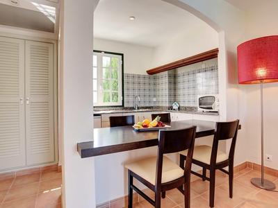 Petite cuisine avec deux chaises en bois, bol de fruits et lampe sur pied rouge