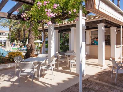 Café en plein air avec tables et chaises blanches à côté d'une piscine et de palmiers.