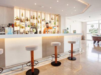 Bar d'hôtel lumineuse avec tabourets blancs, comptoir éclairé et ambiance élégante.