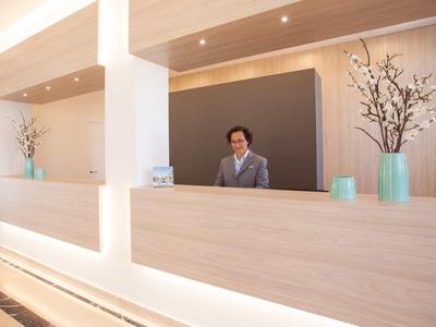 Un réceptionniste amical à une réception d'hôtel moderne avec du bois clair et des décorations.