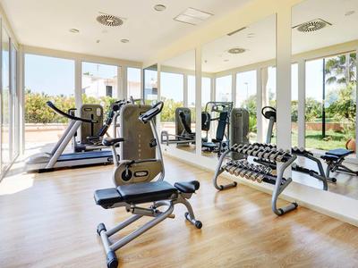 Gimnasio luminoso con equipos modernos y grandes ventanas con vistas a la vegetación.
