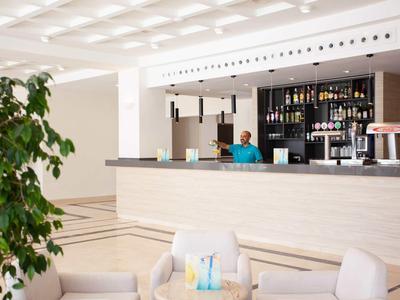 Bar d'hôtel moderne avec comptoir clair, barman et coin salon confortable au premier plan.