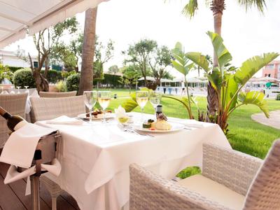 Ein gedeckter Tisch mit Wein und Gläsern auf einer Terrasse mit Blick auf einen grünen Garten und Palmen.