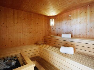 Salle de sauna avec panneaux et bancs en bois clair, décorée avec des serviettes blanches.