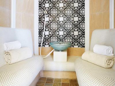 Espace sauna avec deux bancs blancs, serviettes roulées et un lavabo devant un mur à motif.