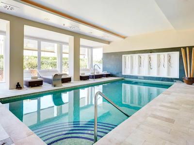 Piscine intérieure moderne avec de grandes fenêtres et des chaises confortables au bord.
