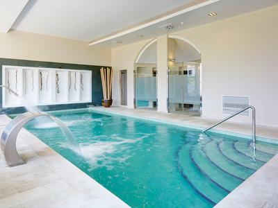 Piscine intérieure moderne avec escaliers, jets d'eau et murs lisses aux tons neutres.