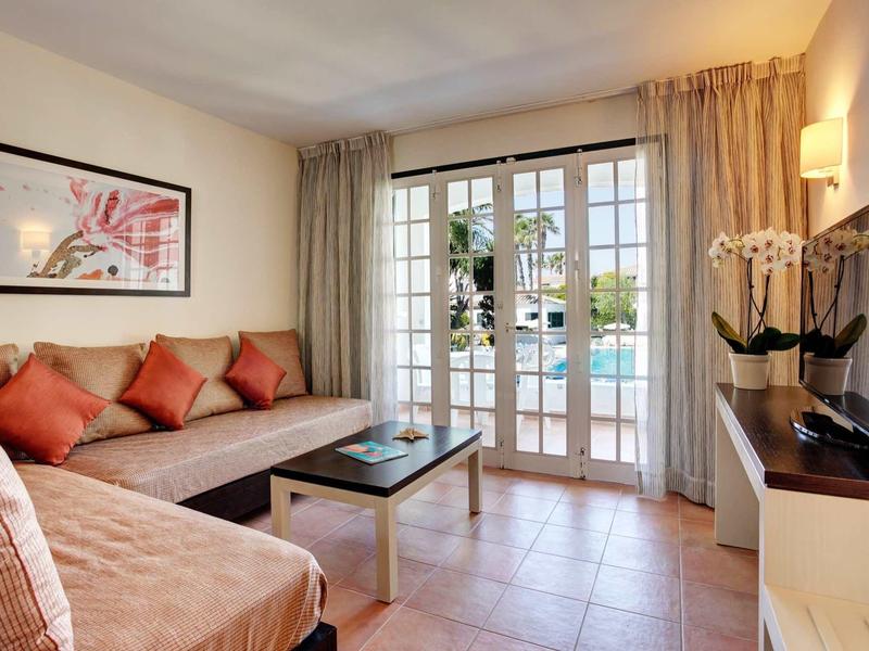 Salon lumineux avec canapé, table basse et vue sur la piscine à travers de grandes fenêtres.