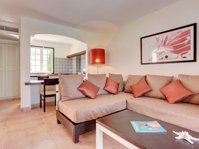 Salon confortable avec canapé d'angle, coussins colorés et vue sur la cuisine ouverte dans une maison de vacances.