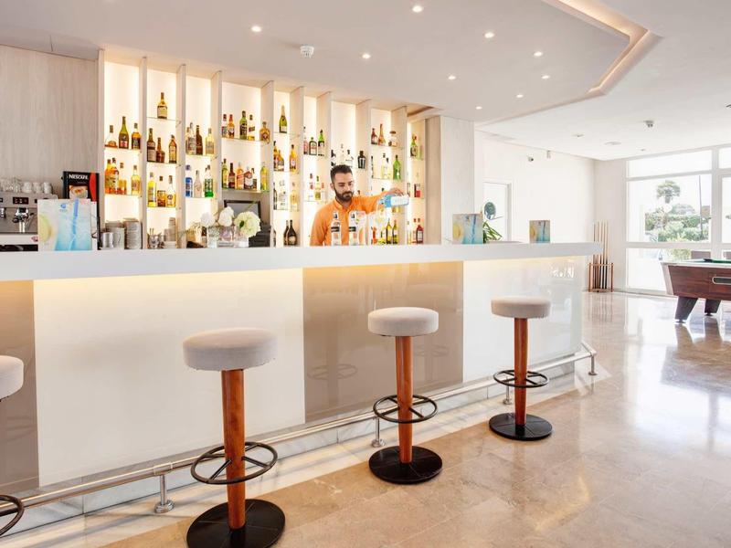 Bar d'hôtel lumineuse avec tabourets blancs, comptoir éclairé et ambiance élégante.