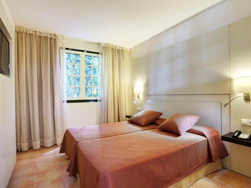 Chambre d'hôtel lumineuse avec deux lits, sol en moquette et fenêtre avec rideaux.