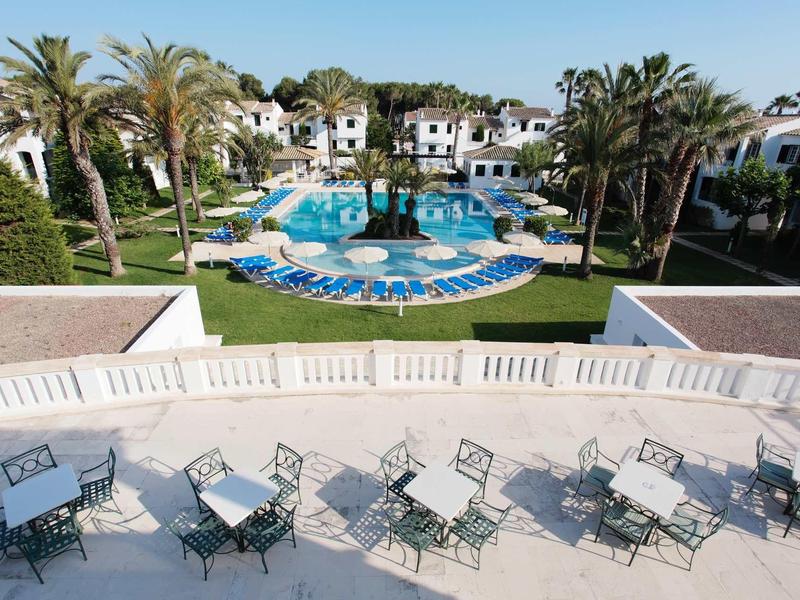 Vue d'une piscine d'hôtel avec espace de sièges et palmiers sous un ciel dégagé
