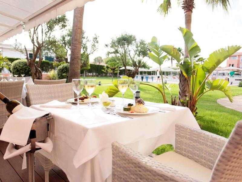 Une table dressée avec du vin et des verres sur une terrasse donnant sur un jardin verdoyant et des palmiers.